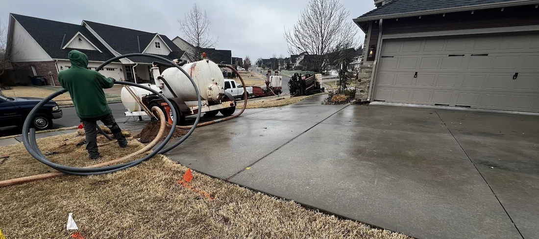 Worker in a residential driveway running a directional bore for a homeowner utility line